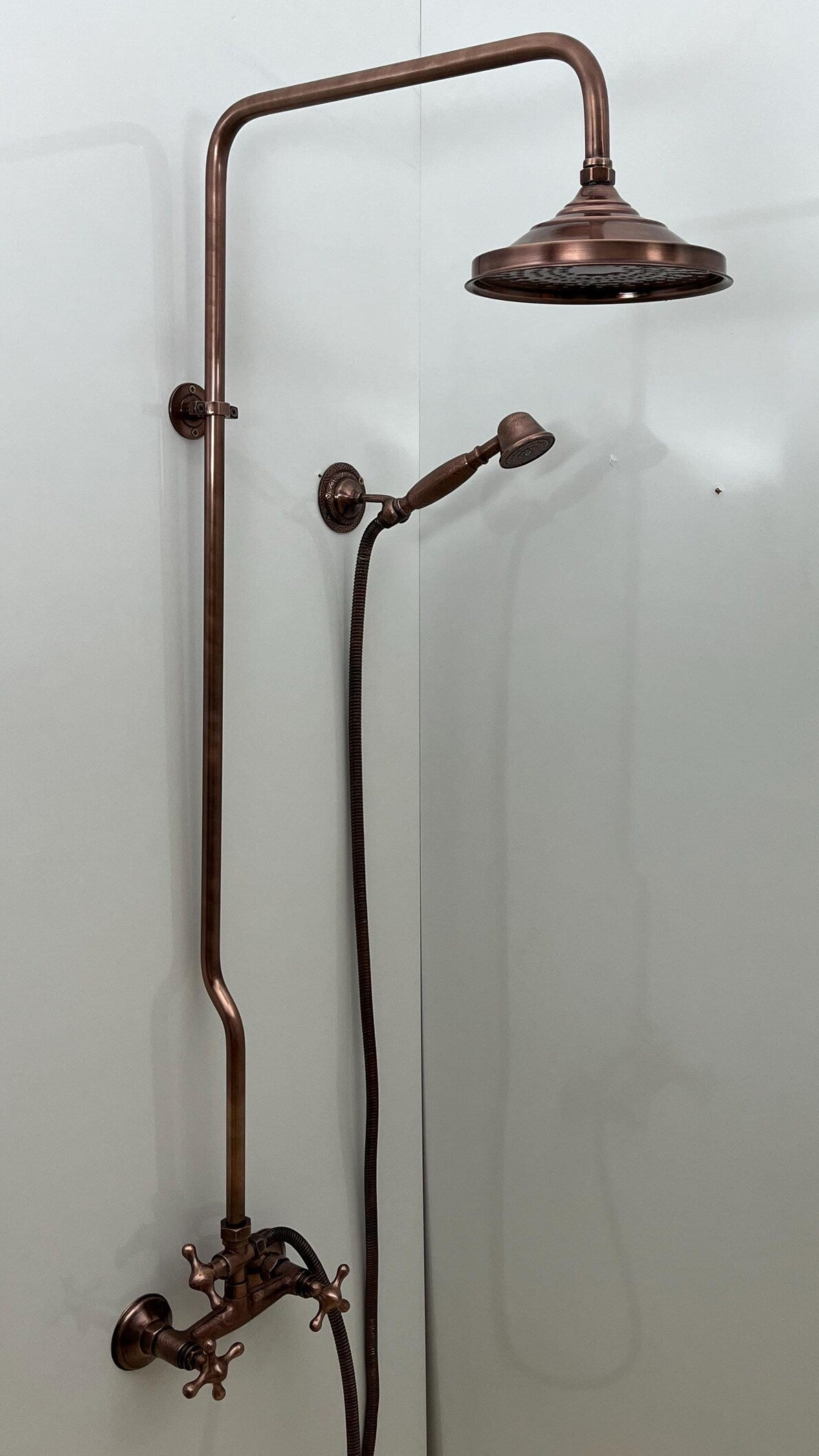 Vintage-style copper shower head and arm mounted on a white wall.